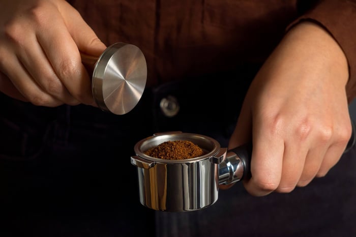 Man tamping ground coffee into espresso machine portafilter basket