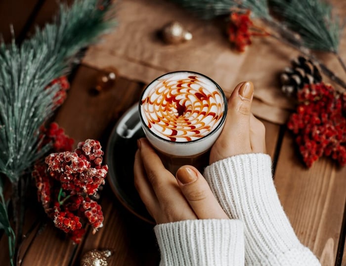 woman holding coffee cup on table surrounded by holiday decor