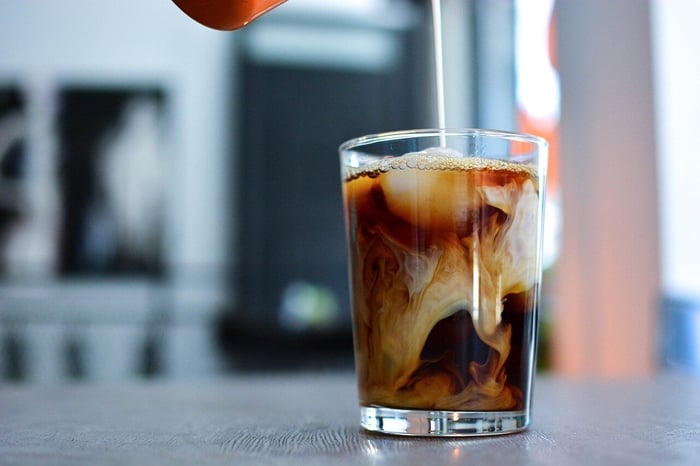 Pouring milk swirling in an iced coffee glass.