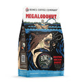 The front of a 12 ounce bag of Bones Coffee Company Megalodonut flavored coffee. It is boston cream donut flavored, and it has a skeleton fishing from a boat using a donut as bait as a donut shark goes to bite the line on the art. 