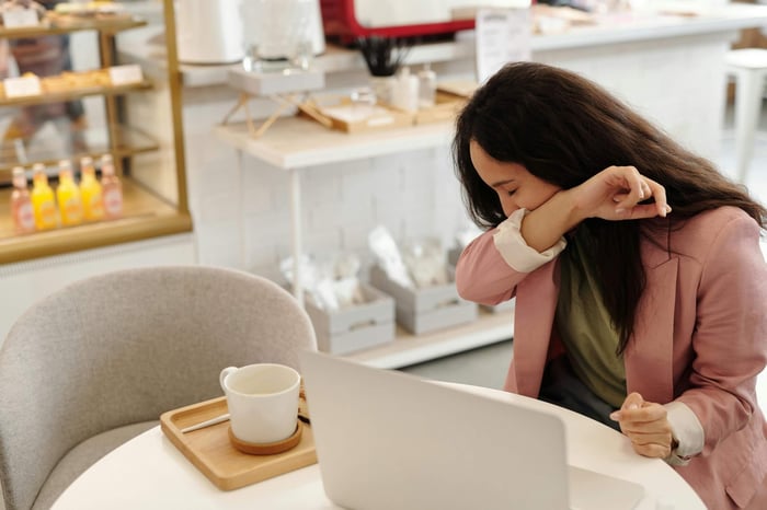 Woman sneezing into elbow while sitting at café workspace