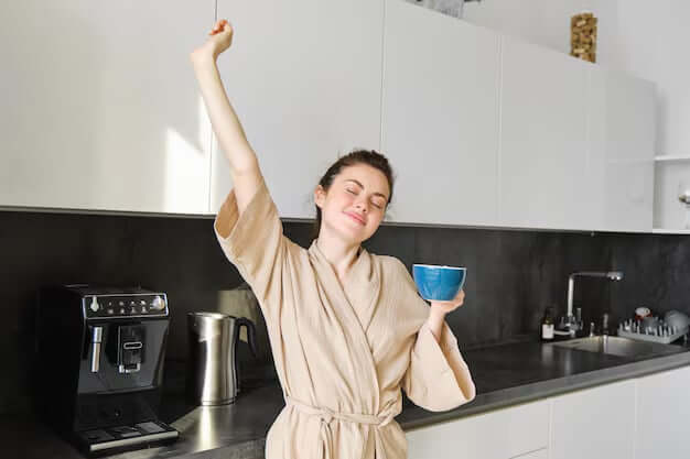 Happy woman holding coffee cup in kitchen. 