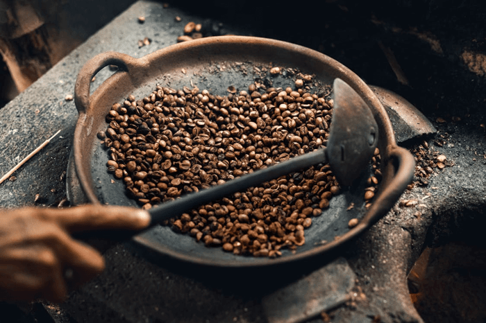 Person roasting coffee beans in rustic cast iron.