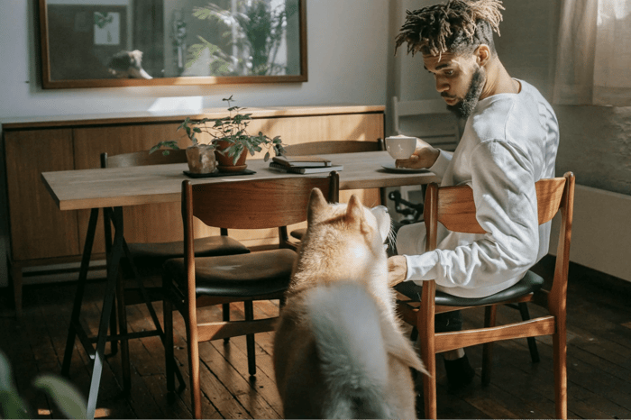 man petting dog while drinking coffee