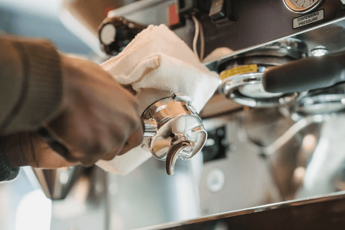 person cleaning an espresso machine portafilter with a cloth